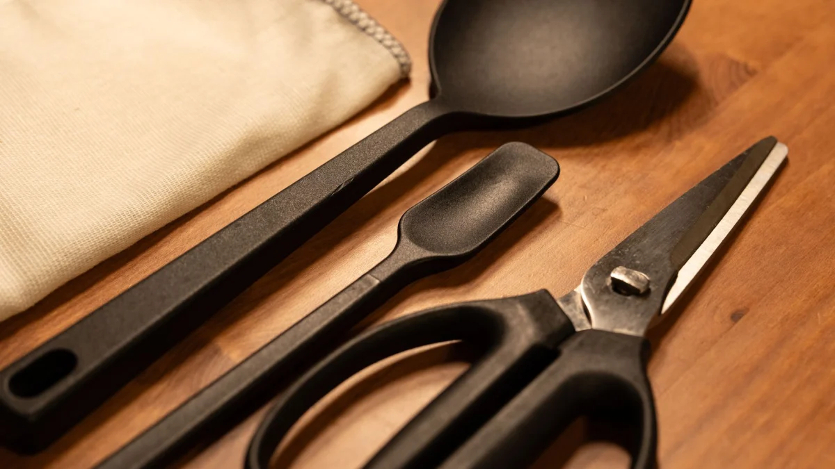 Een set moderne zwarte keukenbenodigdheden, waaronder een schaar, op een houten blad, voor een strakke culinaire stijl.