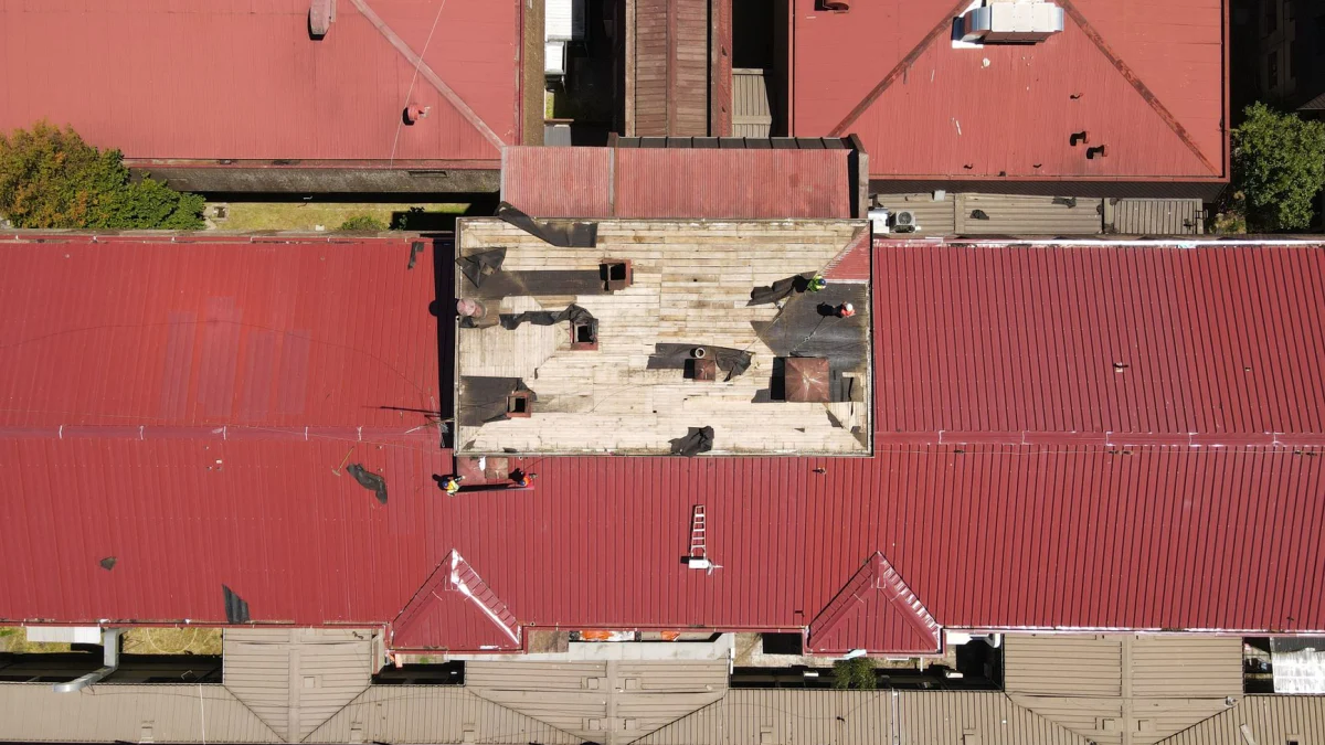 Drone-opname van een stadsbeeld met rode daken en zichtbare werknemers op een zomerse dag.