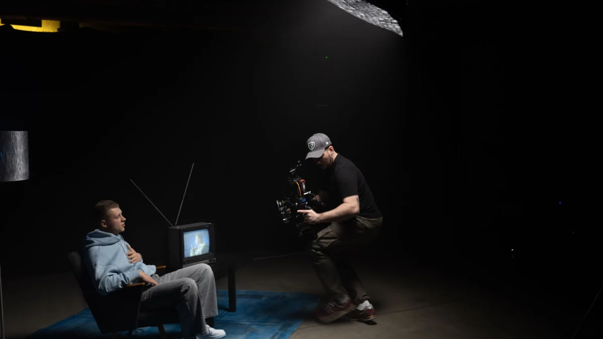 Een fotograaf legt een scène vast waarin een man naast een oude televisie zit in een slecht verlichte studio.