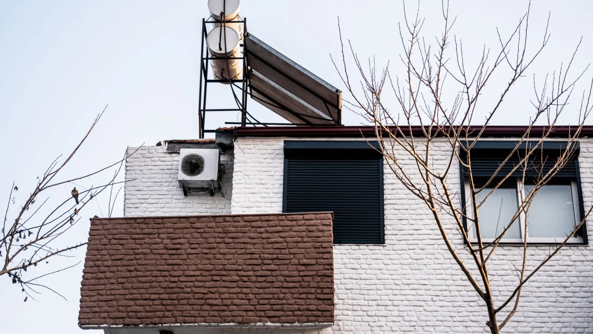 Een minimalistische gevel met airconditioning en kale winterbomen, bekeken vanuit een lage hoek.
